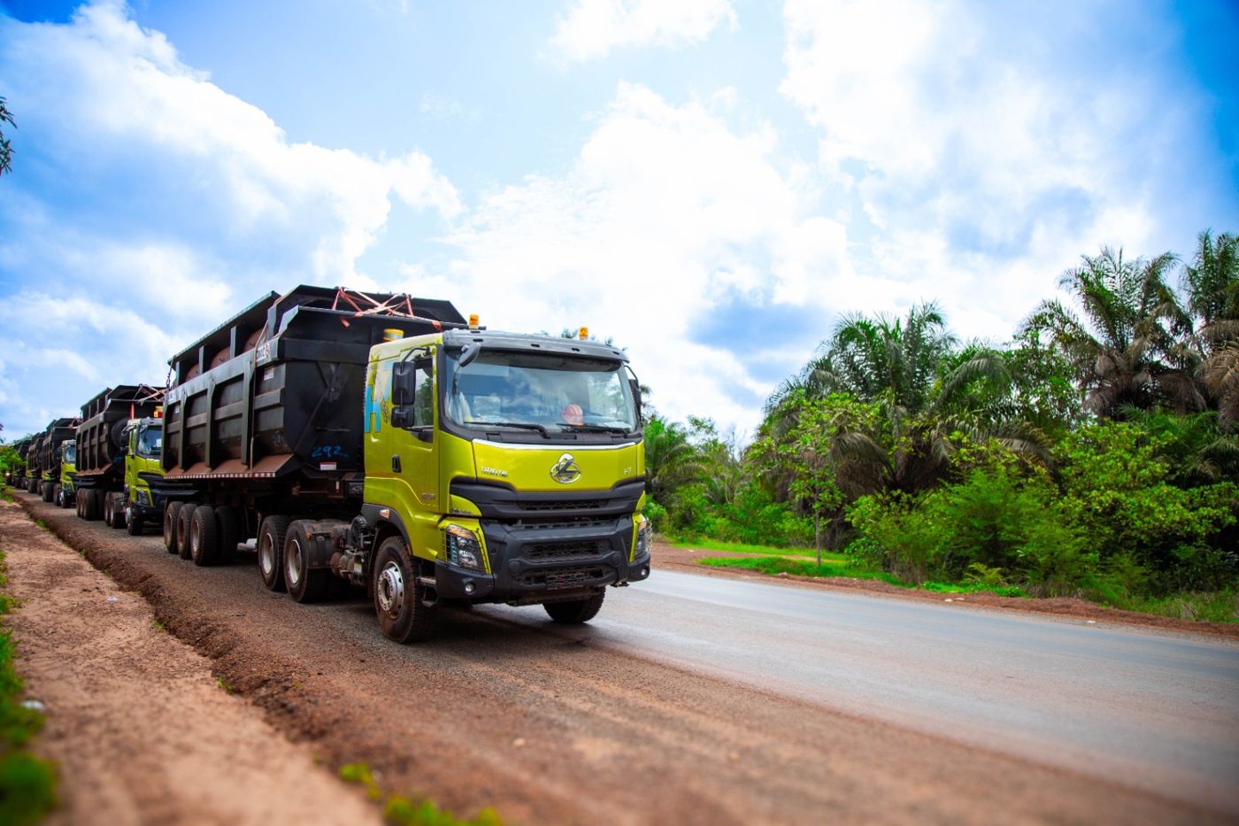 Convoi de camions-bennes SPL sur une route bordée de palmiers